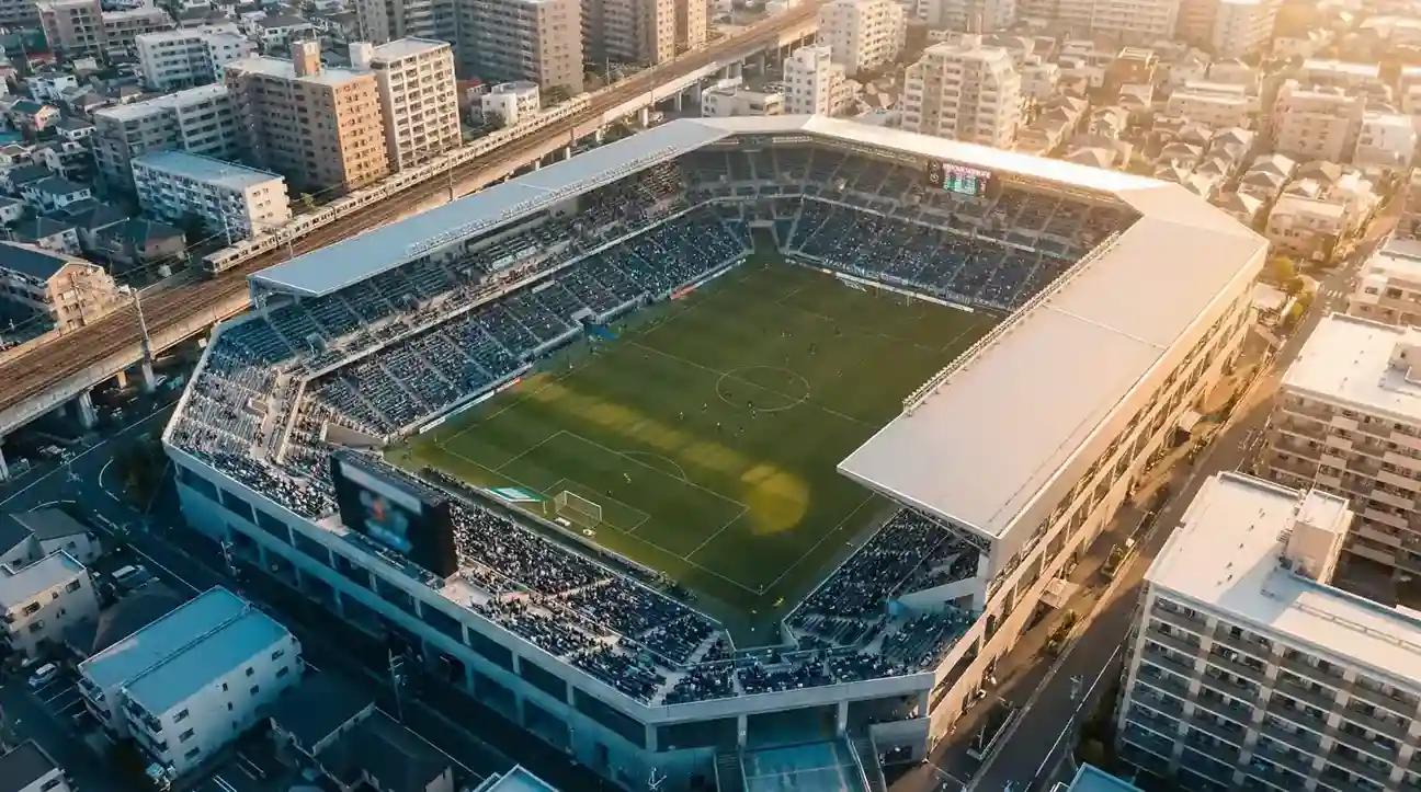 Vista aérea de un estadio japonés de la J-League durante un partido con el campo perfectamente iluminado y las gradas ocupadas